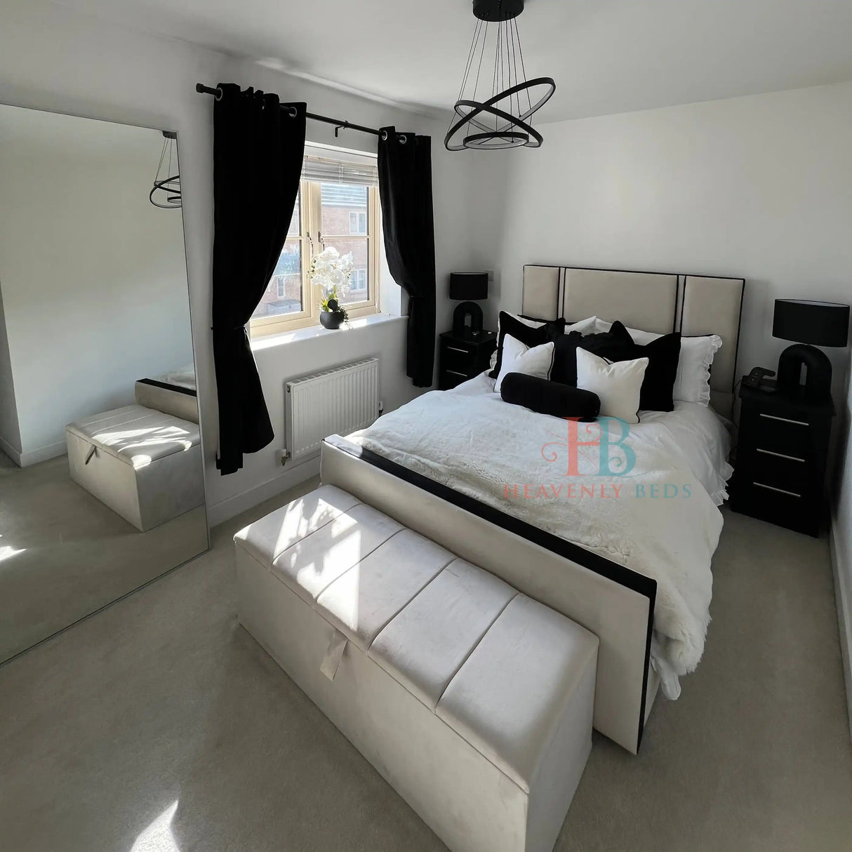 Modern bedroom with a bed, bench, and window with black curtains.